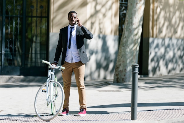 Bel homme africain avec téléphone portable et vélo à pignon fixe dans la rue.