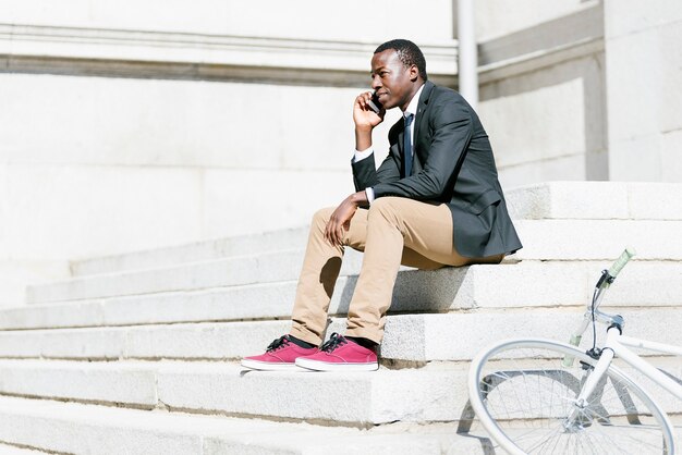 Bel homme africain avec téléphone portable et vélo à pignon fixe dans la rue.