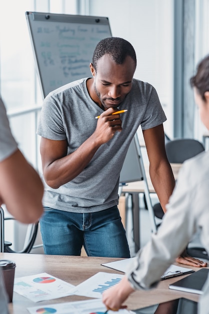 Bel homme afro-américain debout près du bureau et pensant à un nouveau projet d'entreprise