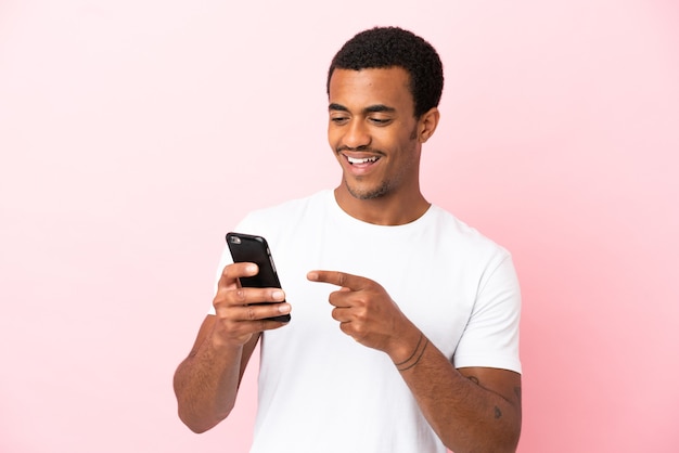 Bel homme afro-américain sur un mur rose isolé envoyant un message ou un e-mail avec le mobile