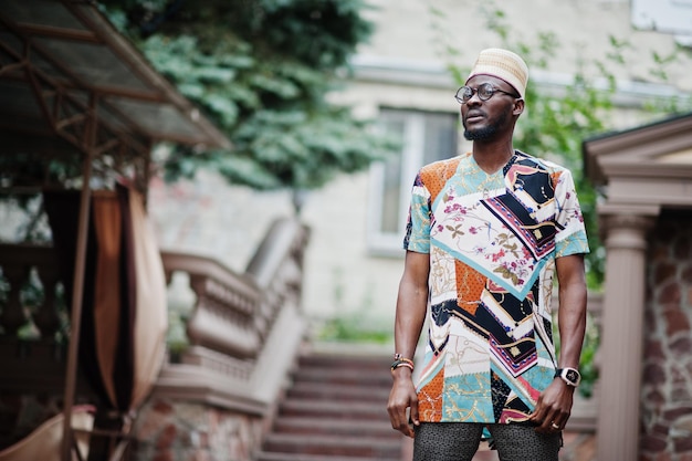 Bel homme afro-américain portant une casquette et des lunettes de vêtements traditionnels dans la ville moderne