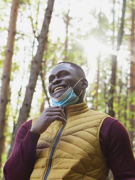 Bel homme afro-américain portant des vêtements décontractés et un masque médical souriant heureux marchant dans le parc de la ville fin de la pandémie