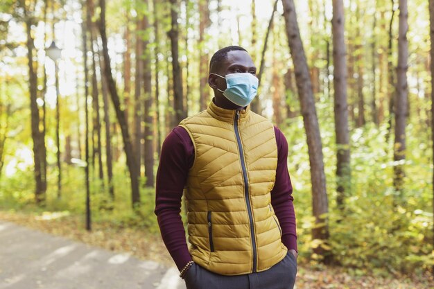 Bel homme afro-américain portant des vêtements décontractés et un masque médical souriant heureux marchant dans