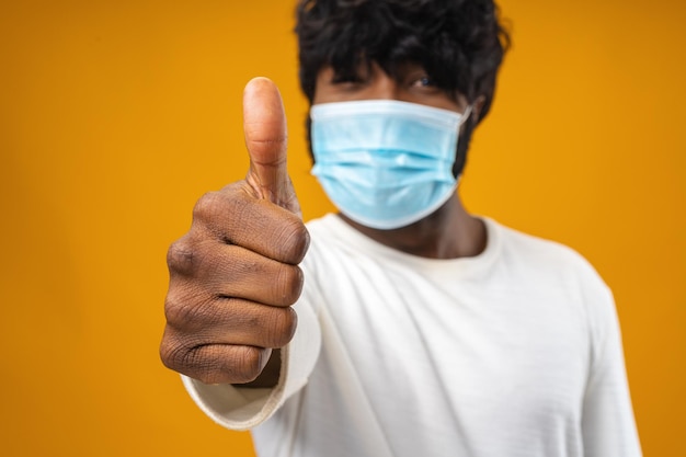 Bel homme afro-américain positif avec masque médical sur fond jaune