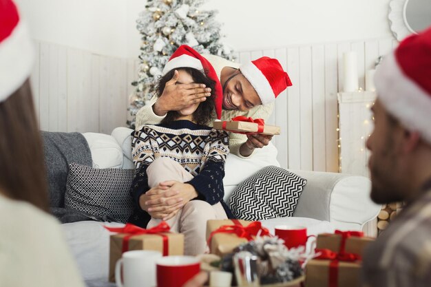 Bel homme afro-américain surprenant petite amie avec cadeau de Noël à la maison, espace de copie
