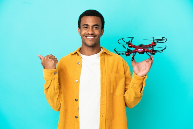 Bel homme afro-américain tenant un drone sur fond bleu isolé pointant sur le côté pour présenter un produit