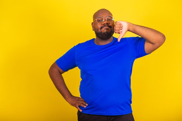 Bel homme afro-brésilien portant des lunettes chemise bleue sur fond jaune pouce vers le bas désapprouvant déception déçu désapprouvant négatif