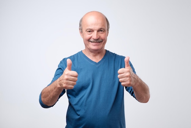 Bel homme âgé en chemise bleue montre le pouce vers le haut