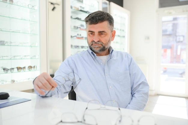 Bel homme âgé choisissant une monture de lunettes dans un magasin d'optique