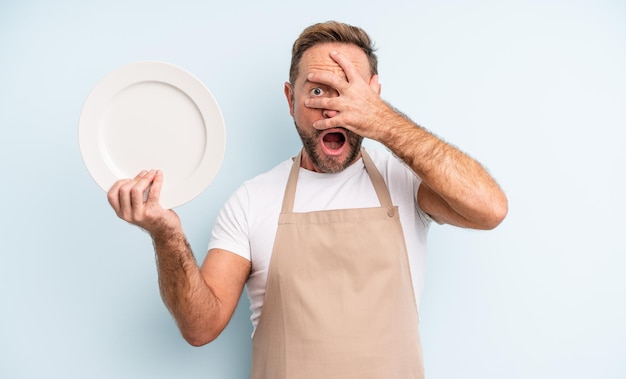 Bel homme d'âge moyen à l'air choqué, effrayé ou terrifié, couvrant le visage avec la main. concept de plat vide