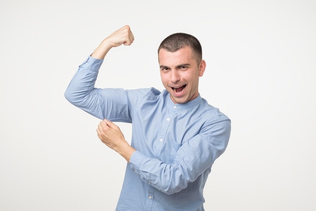 Bel homme d'âge moyen en chemise bleue pointant les biceps exprimant la force et la vie saine