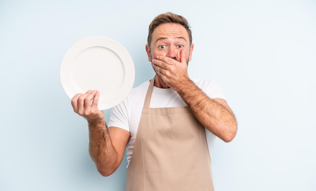 Bel homme d'âge moyen couvrant la bouche avec les mains avec un choc. concept de plat vide