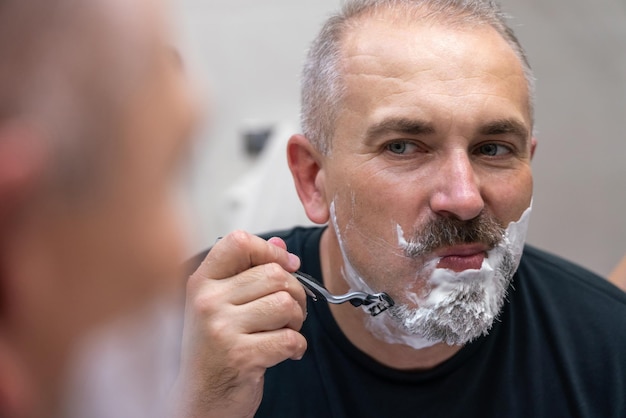 Bel homme d'âge moyen se rasant la barbe dans la salle de bain