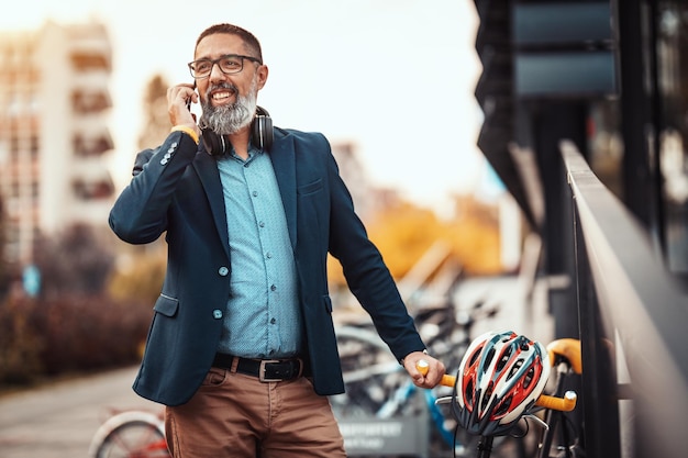 Un bel homme d'âge moyen se rend au travail à vélo et parle sur le smartphone devant le quartier des bureaux.