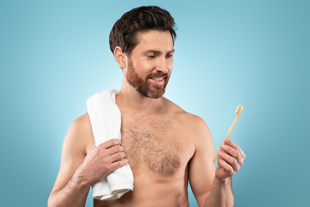 Bel homme d'âge moyen avec une serviette sur l'épaule tenant une brosse à dents profitant de l'hygiène bucco-dentaire posant sur