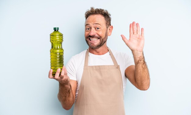 Bel homme d'âge moyen souriant joyeusement, agitant la main, vous accueillant et vous saluant. concept d'huile d'olive