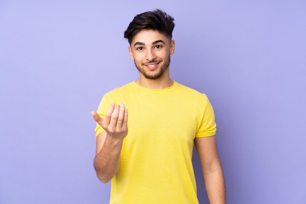 Bel homme arabe sur un mur isolé invitant à venir avec la main.