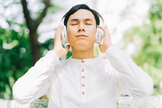 Bel homme asiatique appréciant la musique dans le parc