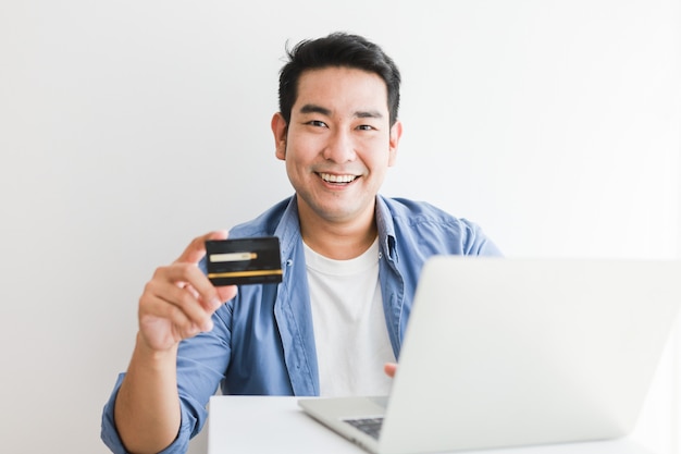 Bel homme asiatique en chemise bleue à l'aide d'une carte de crédit avec un ordinateur portable shopping en ligne