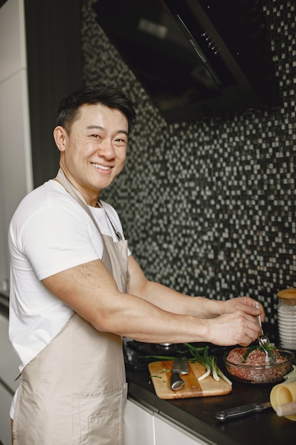 Bel homme asiatique cuisine à la maison. Homme préparant la viande dans la cuisine.