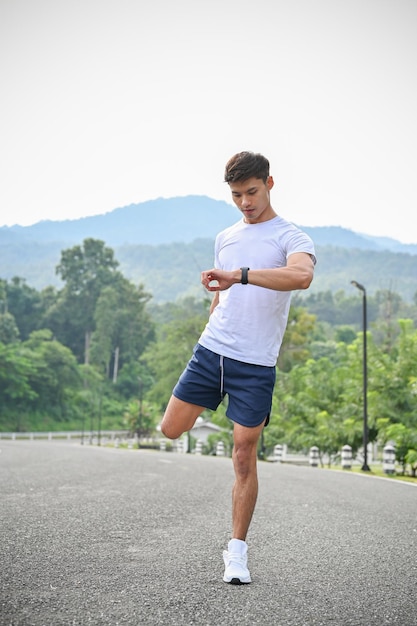 Bel homme asiatique étirant ses jambes en regardant sa montre de sport intelligente