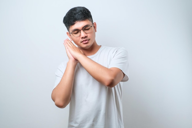 Bel homme asiatique portant une chemise endormie fatiguée rêvant et posant avec les mains ensemble tout en souriant les yeux fermés