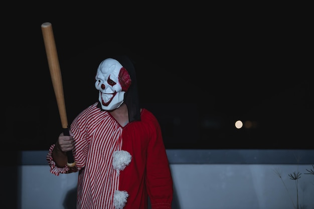 Un bel homme asiatique porte un masque de clown avec une arme sur la scène de nuit Concept de festival d'Halloween Photo effrayante d'horreur d'un tueur en tissu orange