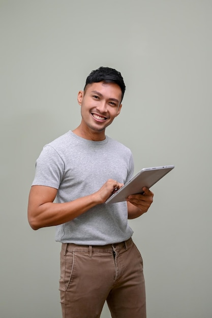 Bel homme asiatique tenant une tablette et debout sur un fond vert isolé