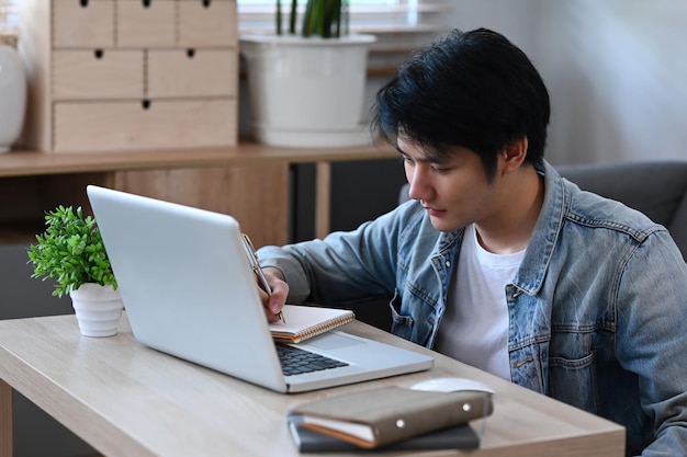 Bel homme asiatique travaillant en ligne sur un ordinateur portable à la maison