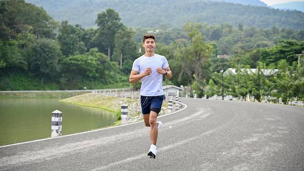 Bel homme asiatique en vêtements de sport courant le long du lac faisant du jogging le matin