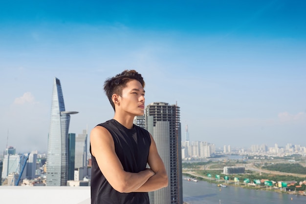 Bel homme asiatique avec des vêtements de sport debout sur le fond de la ville croisant ses bras