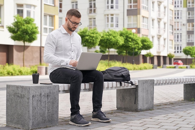 Bel homme assis sur un banc travaillant sur un ordinateur portable à l'extérieur