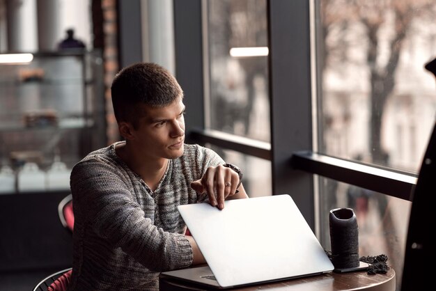 Bel homme assis dans un café près de la fenêtre avec un ordinateur portable