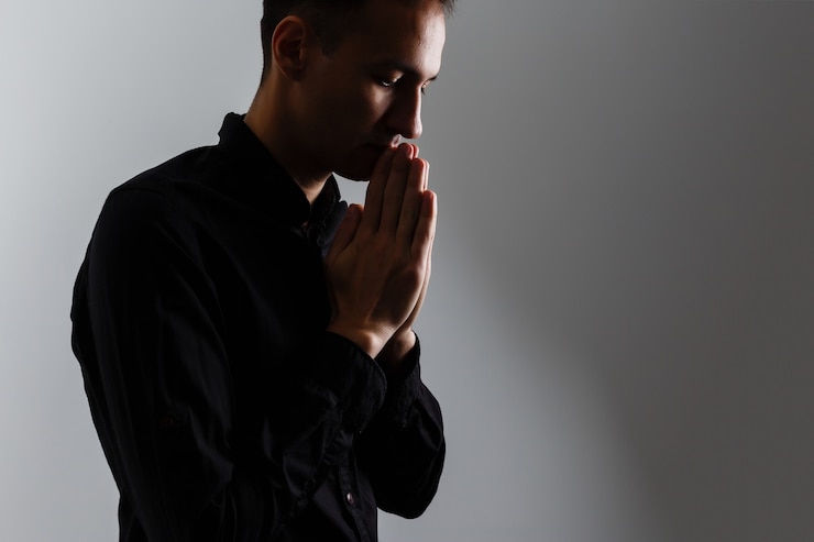 Bel homme assis prière sur fond noir. Ses mains prient pour les bénédictions de Dieu.