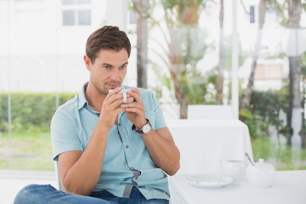 Bel homme assis à table ayant un café