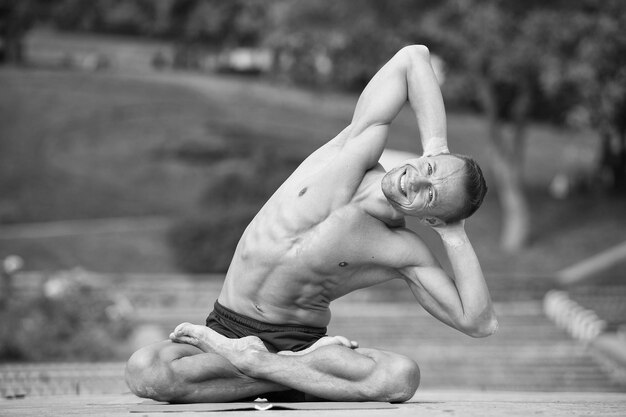 Bel homme athlétique faisant des asanas de yoga dans le parc