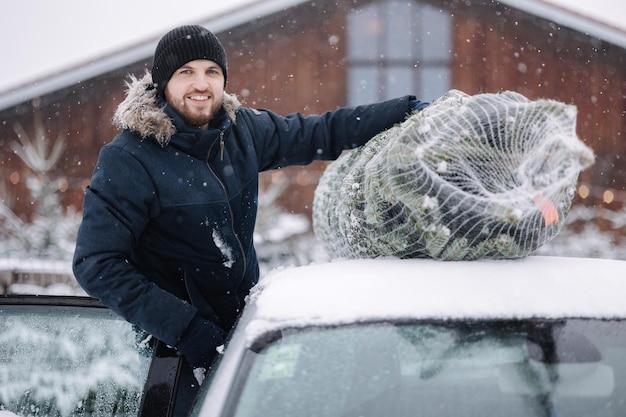 Bel homme attachant à mettre un sapin de noël sur le toit de la voiture pour le ramener à la maison sapin vivant