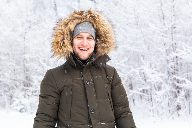 Bel homme au chapeau d'hiver souriant portrait sur la nature enneigée.