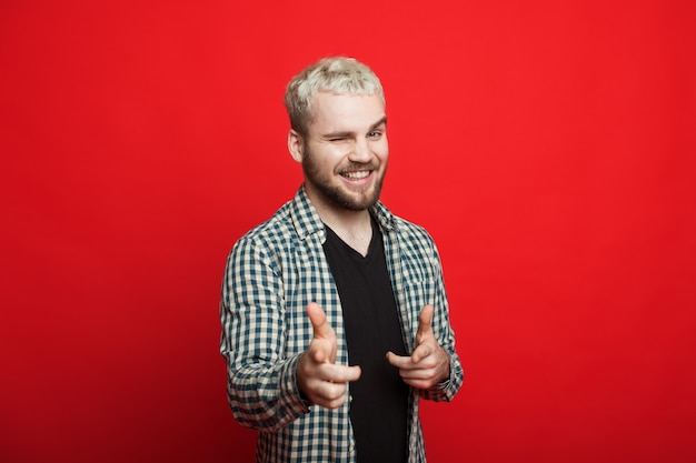 Bel homme aux cheveux blonds et à la barbe pointe vers la caméra tout en clignotant