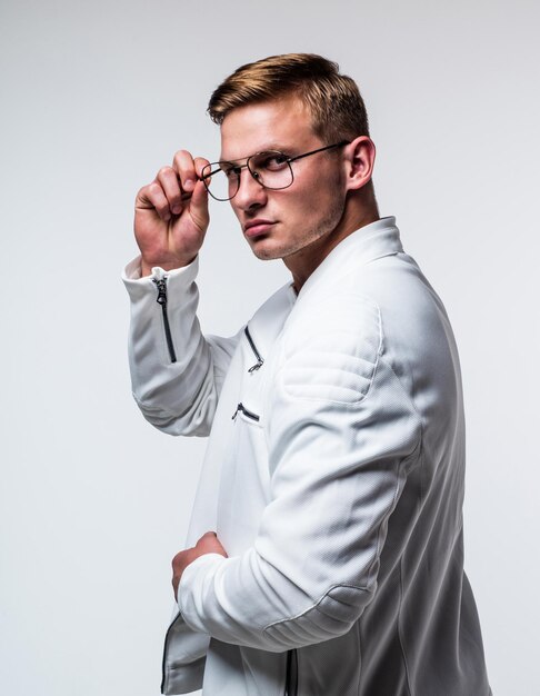 Bel homme aux cheveux blonds courts à la mode porter des lunettes correctrices fixes avec un regard sérieux isolé sur la vue blanche