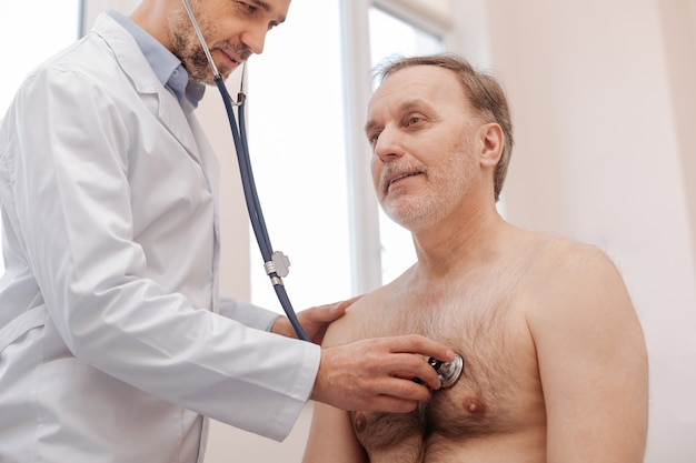 Bel homme aux cheveux gris à la retraite assis au bureau du médecin et faisant ce qu'il dit en attendant son diagnostic