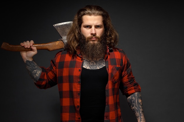 Bel homme aux cheveux longs avec une hache dans les mains sur un fond de studio sombre.