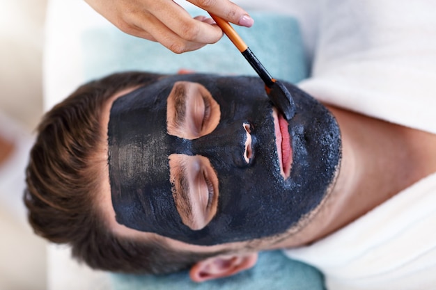 bel homme ayant un soin du visage dans un salon spa