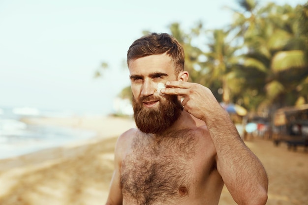 Bel homme avec barbe dans des lunettes de soleil prenant un bain de soleil avec un corps de lotion solaire en été