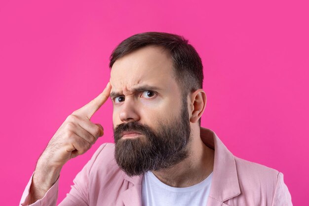 Bel homme avec une barbe dans une veste rose réfléchit sur un fond rouge isolé