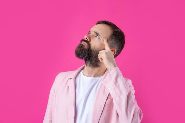 Bel homme avec une barbe dans une veste rose réfléchit sur un fond rouge isolé