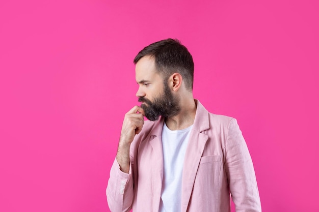 Bel homme avec une barbe dans une veste rose réfléchit sur un fond rouge isolé