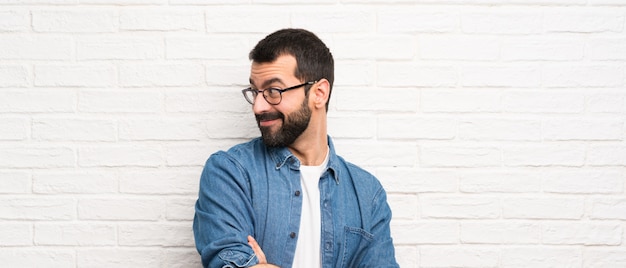 Bel homme à la barbe sur mur de briques blanches avec bras croisés et heureux