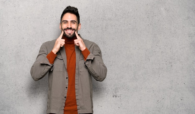 Bel homme à la barbe souriant avec une expression heureuse et agréable sur un mur texturé