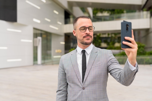 Bel homme barbu chauve hispanique prenant selfie avec des lunettes dans la ville en plein air